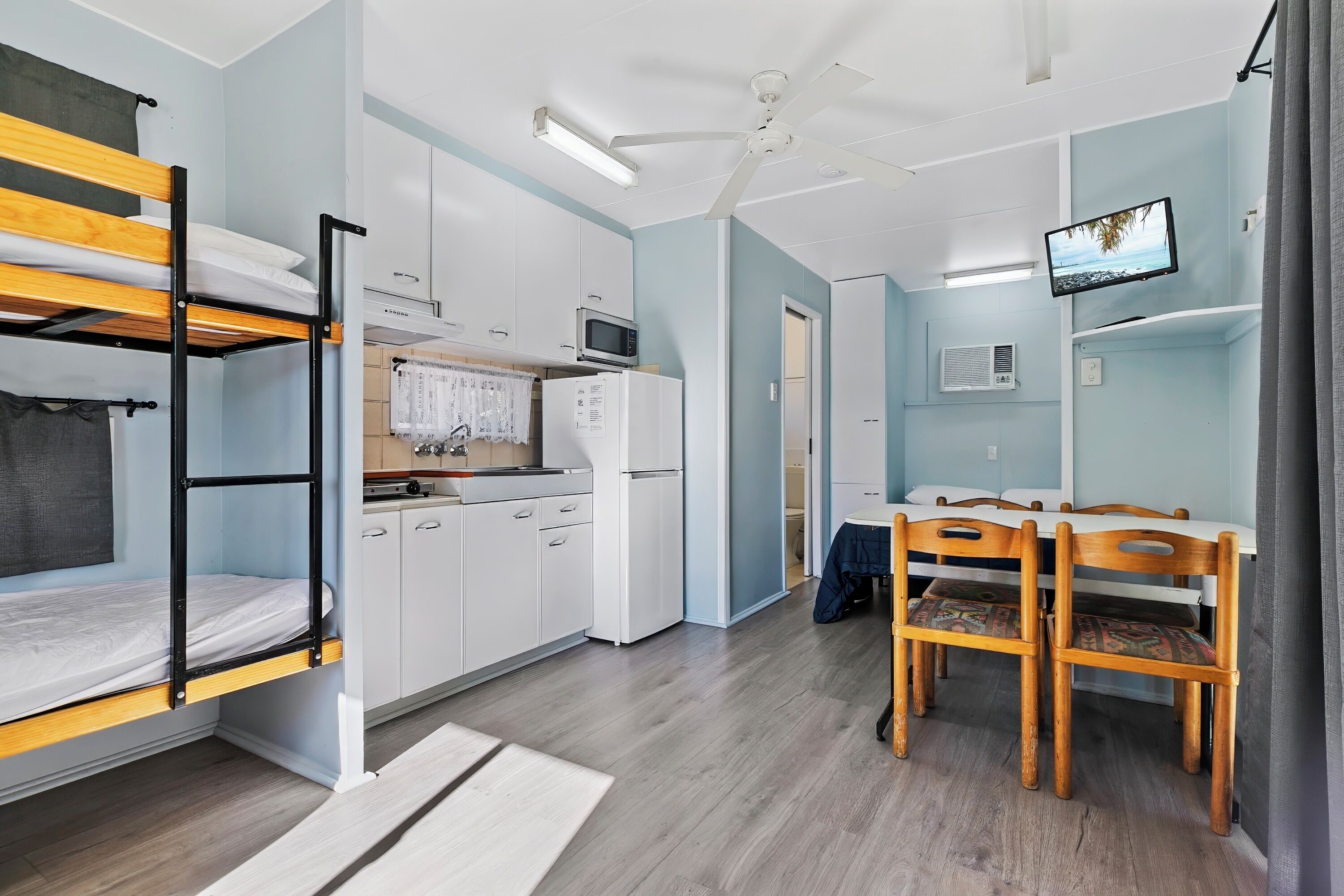 A compact room with bunk beds, a kitchenette, a dining area, and a TV.