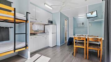 A compact room with bunk beds, a kitchenette, a dining area, and a TV.