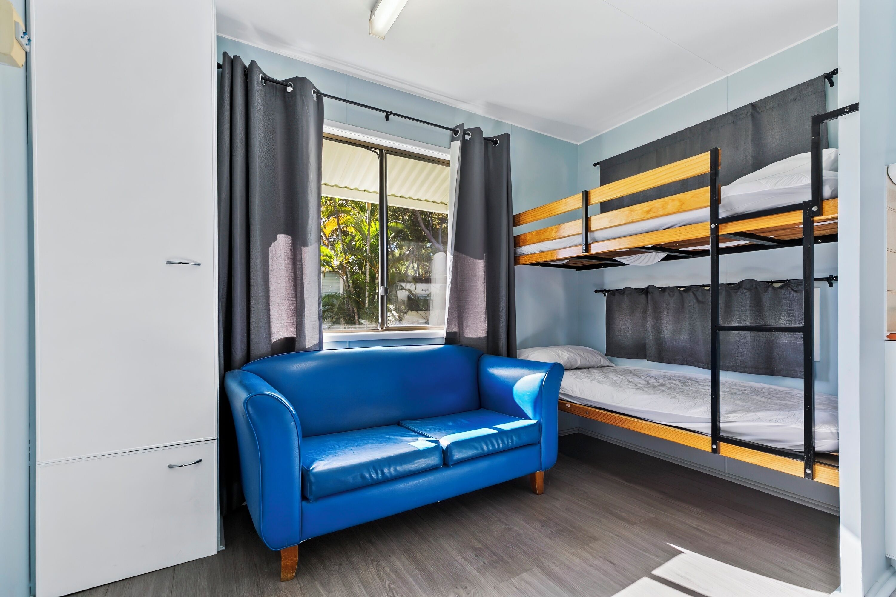A compact room with a bunk bed, a blue sofa, and a window with curtains.
