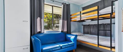 Una habitación pequeña con una cama litera, un sofá azul y una ventana con cortinas.