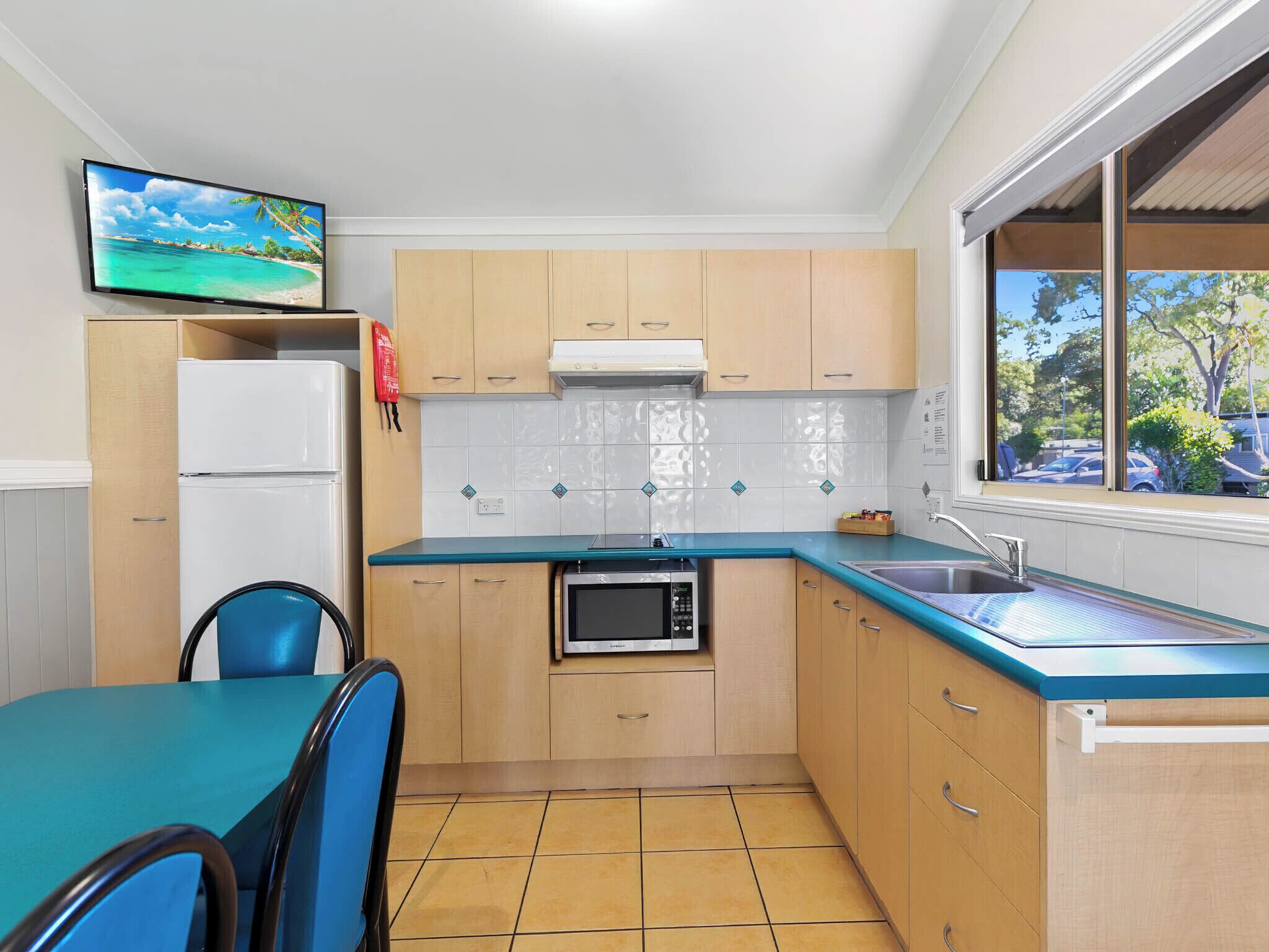 A compact kitchen with a refrigerator, microwave, and sink. There is a dining table with chairs and a window with a view of the outside.