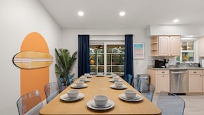 Un comedor moderno con una mesa de madera preparada para ocho personas, rodeada de sillas de vidrio transparente.
