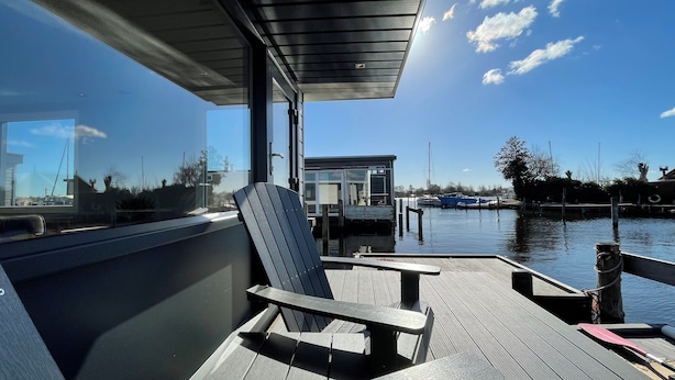 Une terrasse avec des chaises et une table, donnant sur une étendue d’eau calme où se trouvent des bateaux.