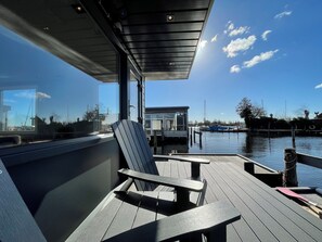 Una terraza con sillas y una mesa, con vista a una masa de agua tranquila donde hay barcos.
