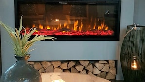 Un salon moderne avec une cheminée, une table basse ronde en bois, un vase avec une plante et un porte-bougie décoratif.