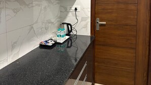 Une cuisine avec un pare-feu en marbre, une porte en bois et un plan de travail sur lequel se trouvent une bouilloire et des bouteilles d’eau.