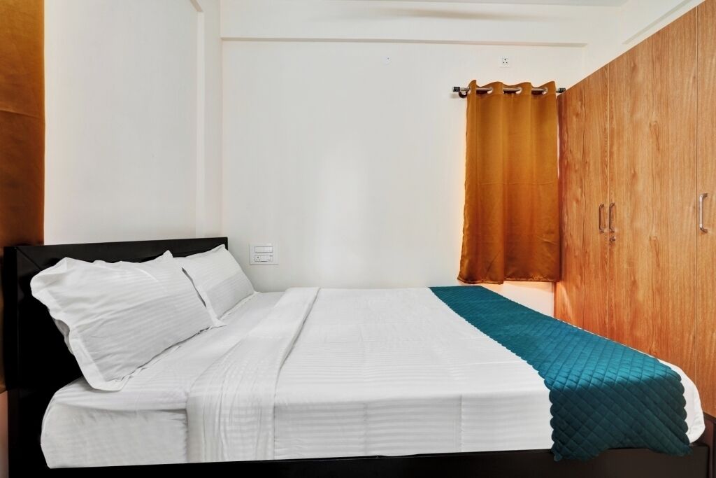A single bed with white bedding, a teal throw blanket, and a wooden wardrobe with a curtain.