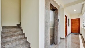 Un intérieur moderne avec un escalier en granit, une porte en bois et un couloir menant à un ascenseur.