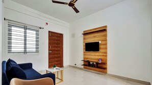 Un salon avec un canapé bleu, un fauteuil marron, un téléviseur fixé au mur en bois et un ventilateur de plafond.