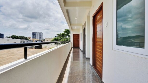 Un couloir avec un balcon, une porte en bois et une vue sur des immeubles et des arbres.