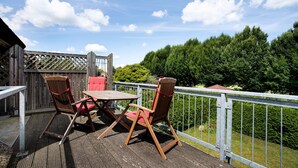 Une terrasse en bois avec une table et deux chaises, une rambarde en métal et une vue sur une forêt.
