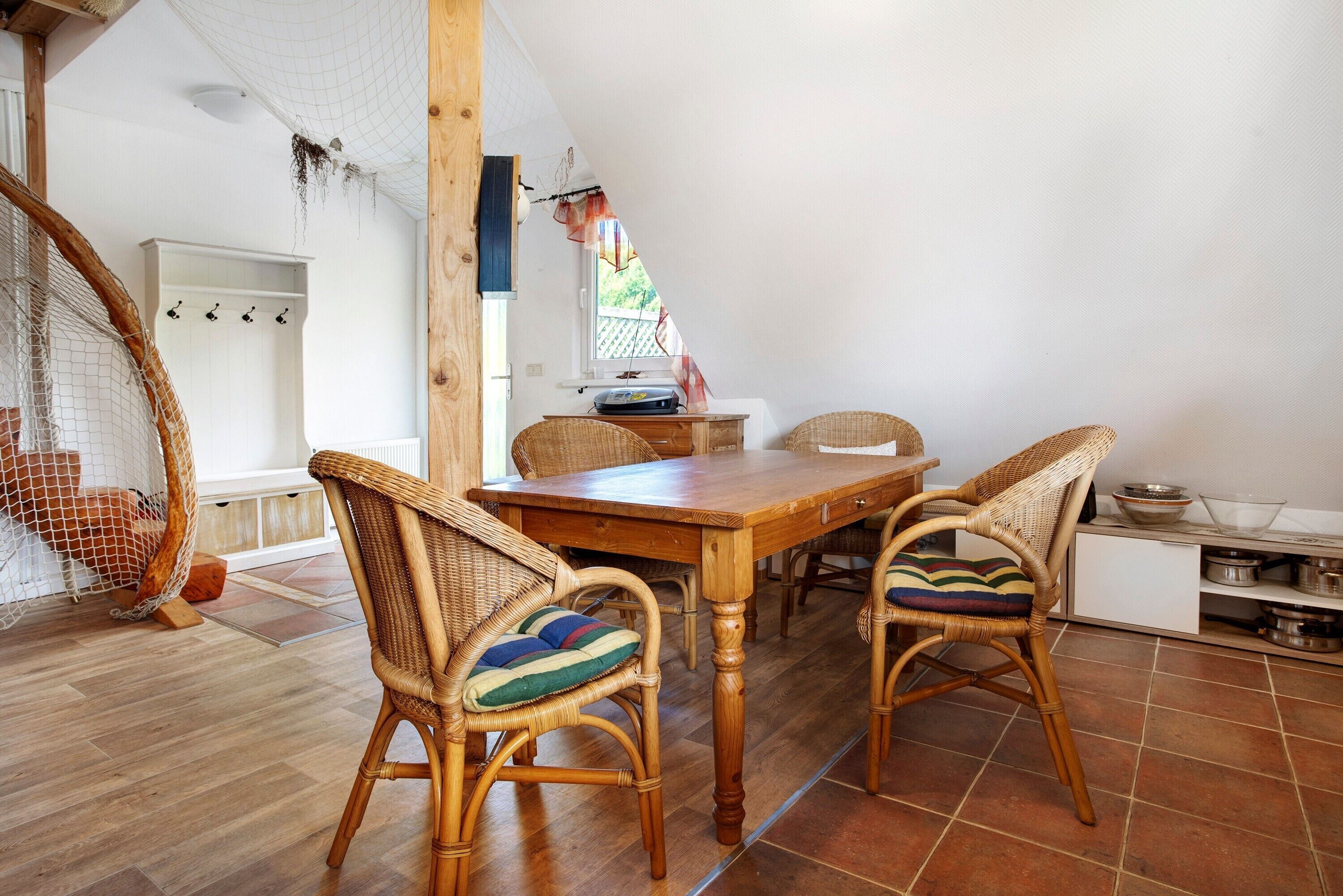 Un comedor con una mesa de madera, sillas de mimbre, un armario blanco y una hamaca colgante.