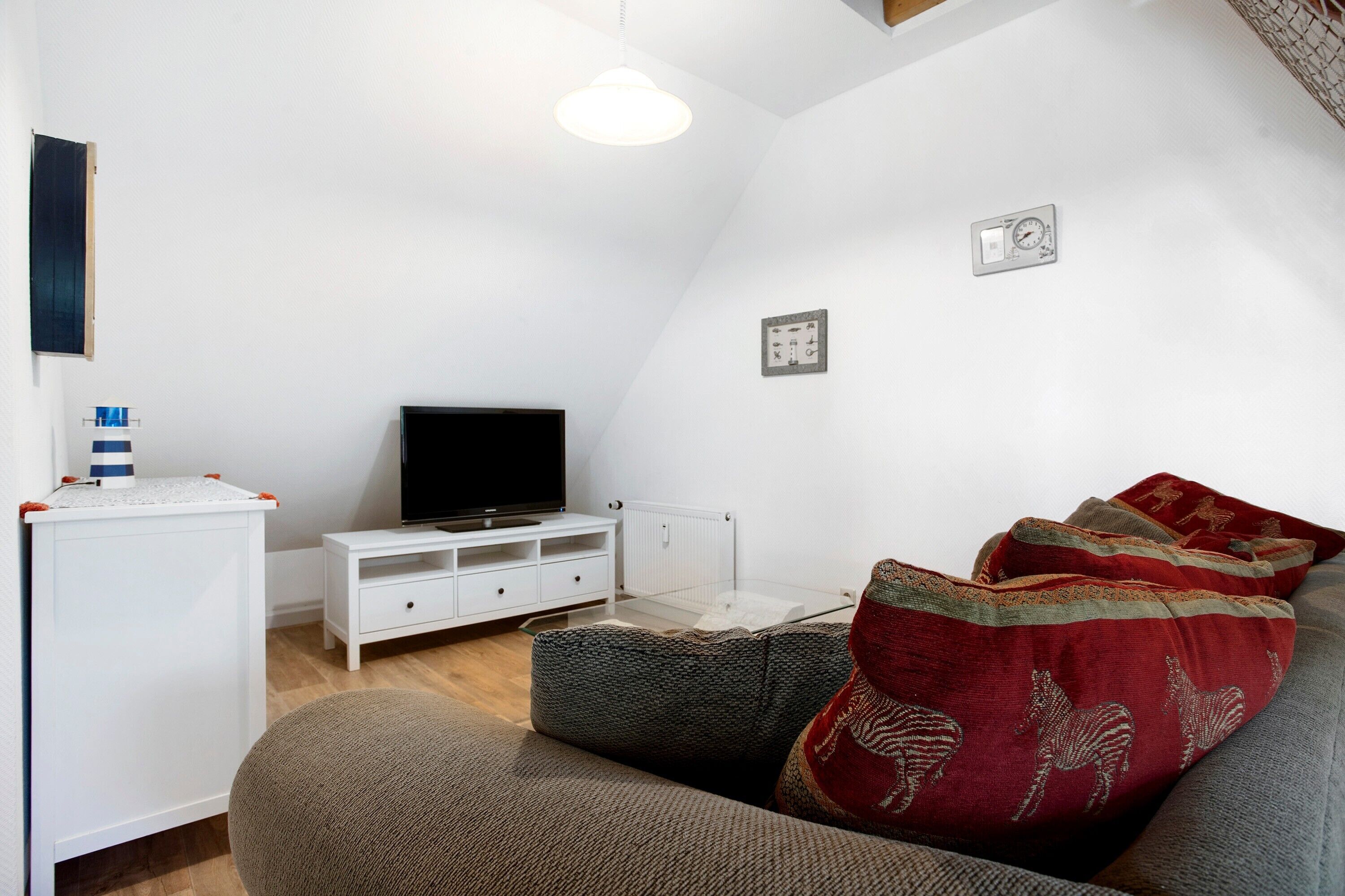 Una sala de estar moderna con un televisor de pantalla plana, muebles blancos y un sofá acogedor con cojines estampados.