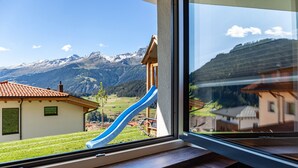 A window view of a mountain landscape with a house and a blue slide. - Apartment 'Berghoamat Nauders' with Mountain View, Private Terrace and Wi-Fi (Nauders)