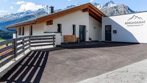 A modern building with a wooden roof and a white facade, a bench, and a mountain view. - Apartment 'Berghoamat Nauders' with Mountain View, Private Terrace and Wi-Fi (Nauders)