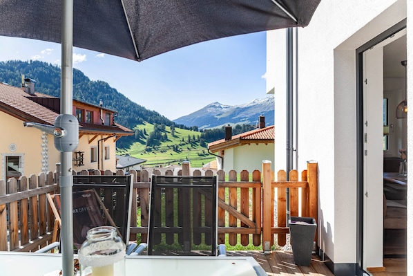 Un balcon donnant sur un paysage montagneux, une clôture en bois et une table sur laquelle se trouve un bocal en verre.