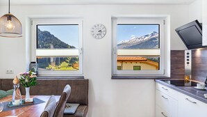 A modern kitchen with two windows, a clock, and a dining area with a table and chairs. - Apartment 'Berghoamat Nauders' with Mountain View, Private Terrace and Wi-Fi (Nauders)