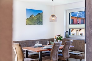Un coin repas avec une table en bois, des chaises rembourrées, un luminaire suspendu et une fenêtre donnant sur un immeuble.