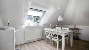 A room with a dining table, chairs, a white radiator, a window with white curtains, and a white ceiling lamp.