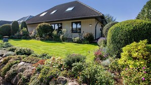 A house with a tiled roof, a well-maintained lawn, and various shrubs and flowers.