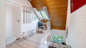 A room with a sloped ceiling, a white door, a chair, a table, and a window with curtains.