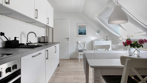 A modern kitchen with white cabinetry, a built-in oven, and a skylight above the dining area.