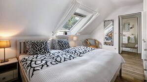 A bedroom with a skylight, a bed with patterned bedding, a nightstand, a chair, and a wardrobe.