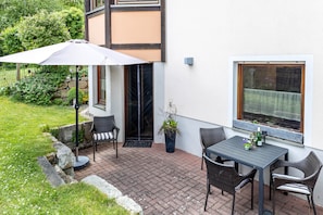 Un patio exterior con una mesa y sillas, una planta en maceta y una ventana con vistas al jardín.