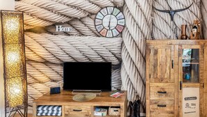 A room with a wooden ceiling, a television on a wooden stand, a wall clock, and a cabinet. - Holiday Apartment 'Quiet Basement Apartment with Terrace' with Private Terrace, Garden, and Wi-Fi (Altenkunstadt)