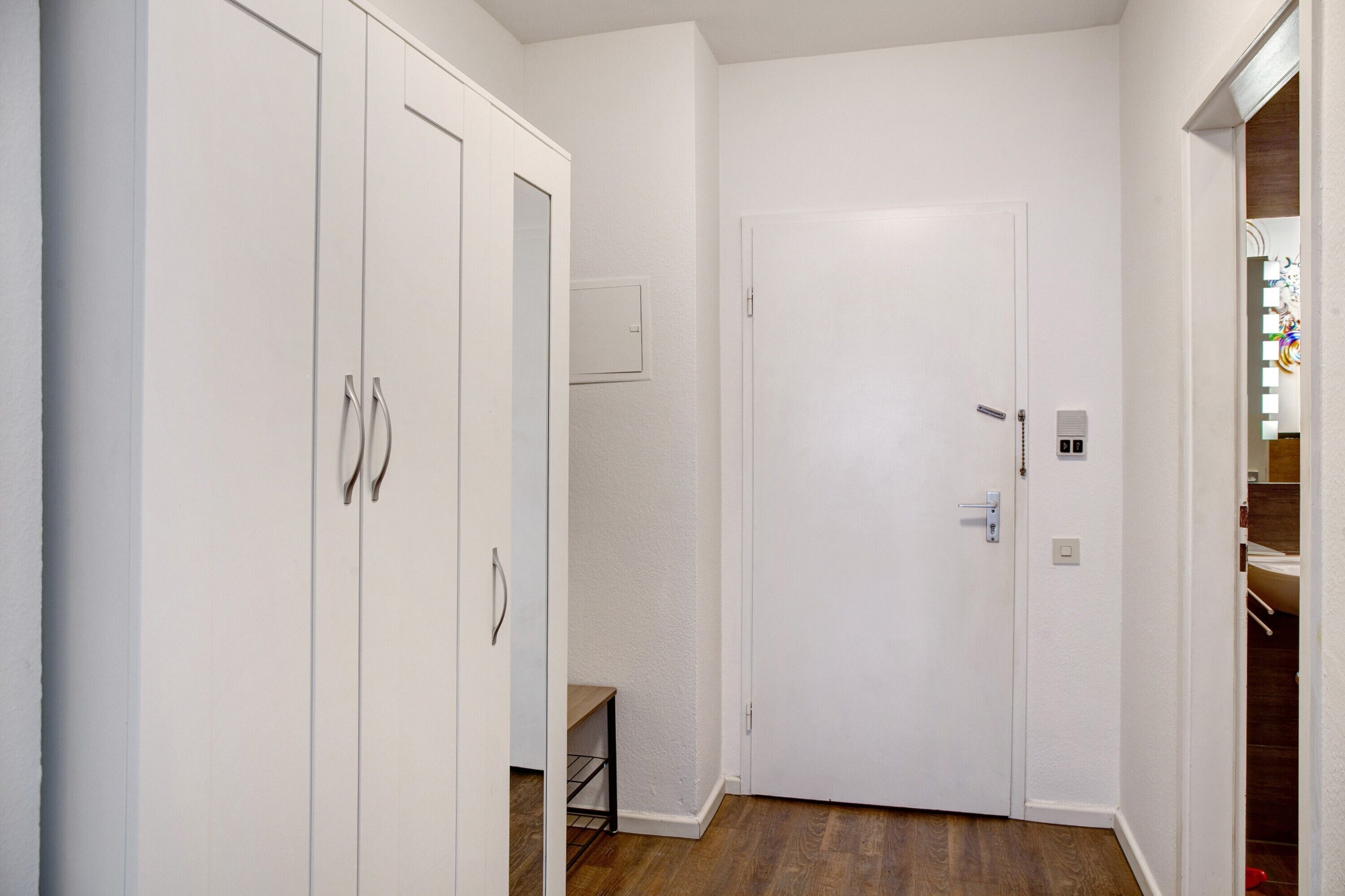 A hallway with white walls, wooden flooring, and a closed door at the end.