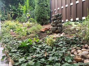 Un jardin agrémenté d’une cascade artificielle en roches, d’un feuillage luxuriant et d’une clôture en bois.