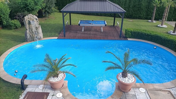 A swimming pool with a gazebo, potted plants, and a stone feature. - Apartment 'Wohlfühloase Ermreuth' with Mountain View, Private Pool and Wi-Fi (Neunkirchen am Brand)