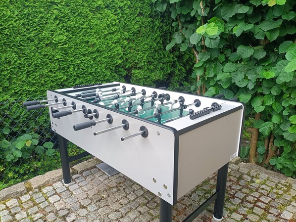 Una mesa de fútbol de mesa al aire libre, con un seto verde de fondo.