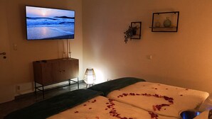 A hotel room with a TV, a cabinet, a bedside table, and two beds with rose petals. - Apartment 'Wohlfühloase Ermreuth' with Mountain View, Private Pool and Wi-Fi (Neunkirchen am Brand)