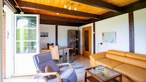Een woonkamer met een houten plafond, een bank, een stoel, een tafel, en een eethoek met stoelen en een tafel.