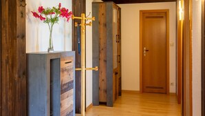 Een gang met houten vloer, een houten deur en een wandrek met bloemen.