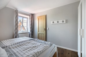 Un dormitorio con dos camas, una ventana con cortinas, una puerta de madera y un interruptor de luz en la pared.