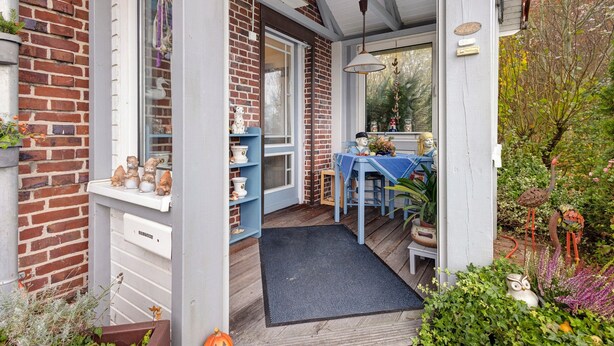 A brick house with a porch, a blue table, and a garden with plants and a bird sculpture. - Holiday Apartment 'Ferienhaus Marchlewski' with Shared Garden and Wi-Fi (Brunsbüttel)