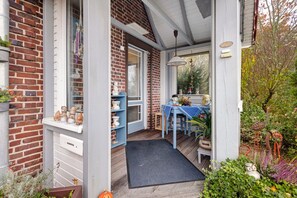 A brick house with a porch, a blue table, and a garden with plants and a bird sculpture. - Ferienhaus 'Marchlewski' mit Gemeinschaftsgarten und WLAN (Brunsbüttel)