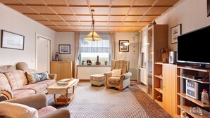 A living room with a sofa, armchair, ottoman, wooden ceiling, and a television. - Holiday Apartment 'Ferienhaus Marchlewski' with Shared Garden and Wi-Fi (Brunsbüttel)