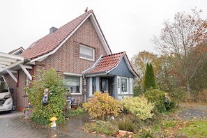 A brick house with a gabled roof, a front porch, and a small garden with various plants and a mushroom decoration. - Holiday Apartment 'Ferienhaus Marchlewski' with Shared Garden and Wi-Fi (Brunsbüttel)