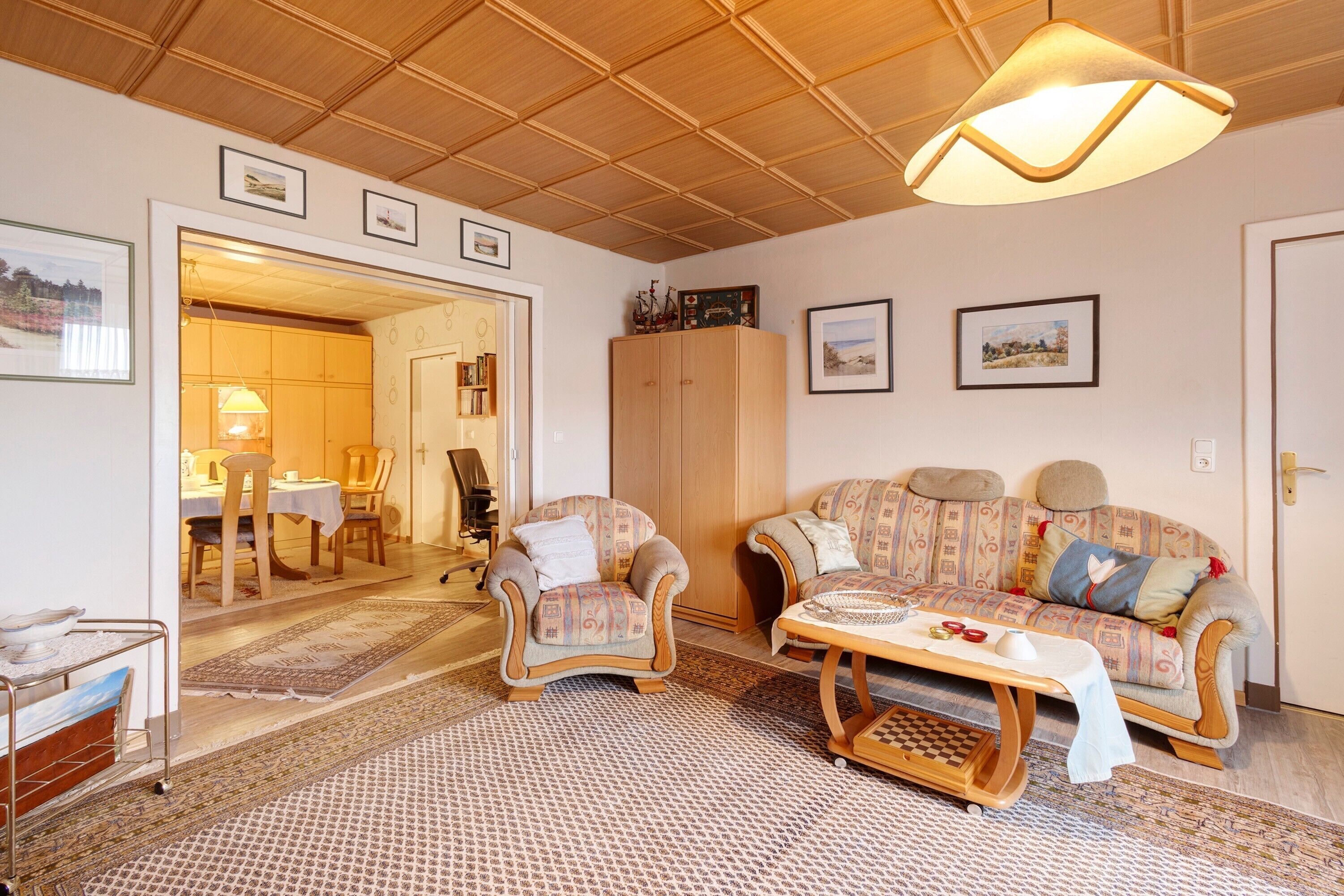Ein gemütliches Wohnzimmer mit Holzboden, einer Couch, einem Sessel, einem Tisch und einer Lampe.