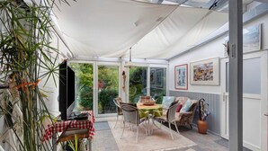 A conservatory with a dining table, chairs, and a large potted plant. - Holiday Apartment 'Ferienhaus Marchlewski' with Shared Garden and Wi-Fi (Brunsbüttel)