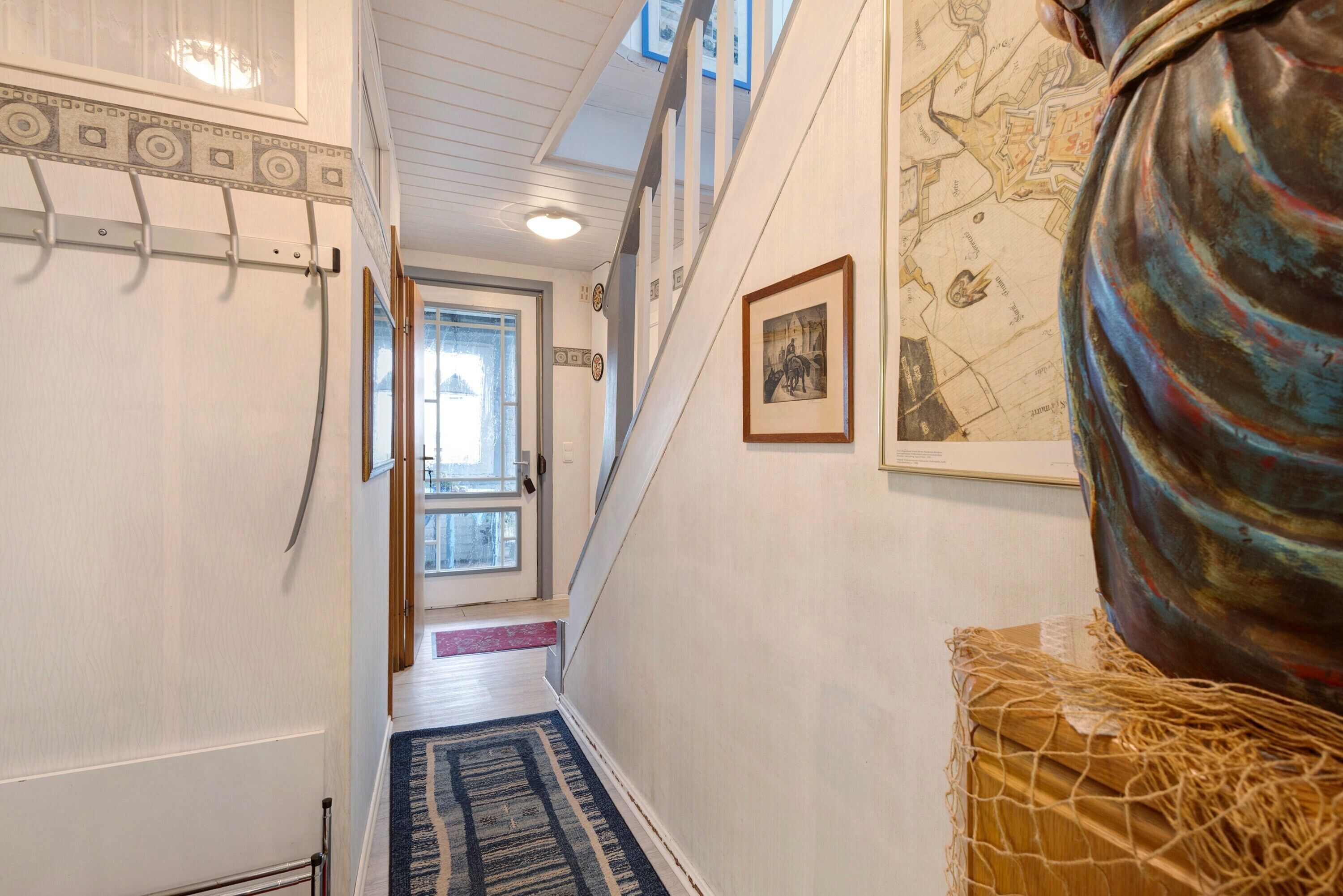 Un couloir avec un tapis à motifs, une carte accrochée au mur et une grande sculpture.