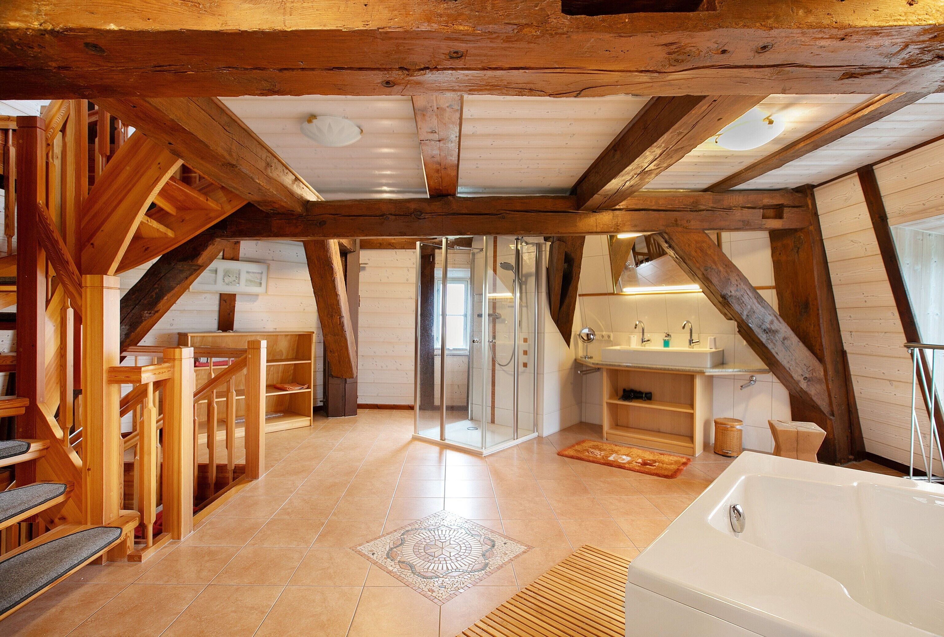 A spacious room with a wooden staircase, a glass shower enclosure, a bathtub, and a small bathroom with a sink and mirror.