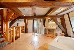 Une pièce spacieuse avec un escalier en bois, une douche en verre, une baignoire et une petite salle de bain équipée d’un lavabo et d’un miroir.