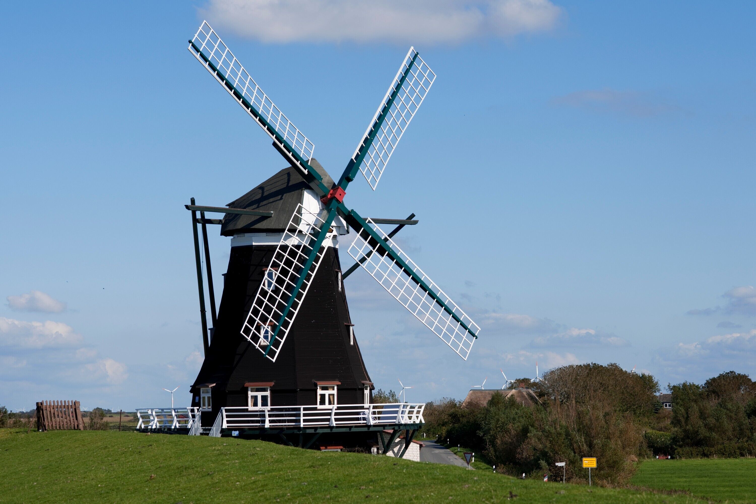 A traditional windmill with a black and white structure, a white fence, and a clear sky.