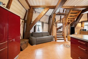 Quarto estilo loft com vigas de madeira aparentes, um armário vermelho, um sofá cinza e uma escada de madeira.
