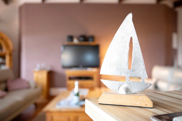 A model sailboat on a wooden stand in a living room with a television and wooden furniture in the background.