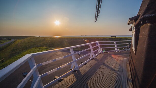 A deck with a railing overlooking a grassy area and a body of water during sunset. - Apartment Müllerwohnung with Terrace (Pellworm)